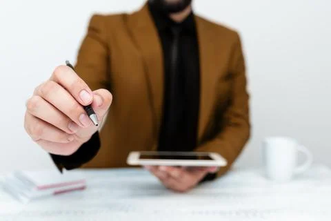 Man in Brown jacket sitting at white table And Pointing With Pen On Important Stock Photos
