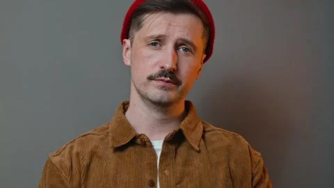 A man in a brown shirt and red beanie shows various expressions while posing 库存影片 337643272