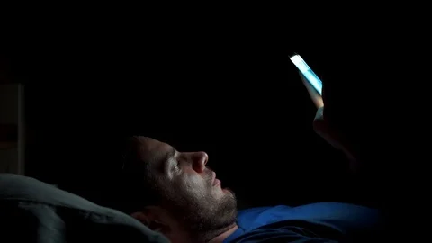 Man browsing the internet on his smartphone in bed in a dark room. Stock Footage 116738778