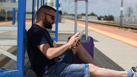 Man browsing internet on tablet while waiting for his train on the station Stock Footage 78653922