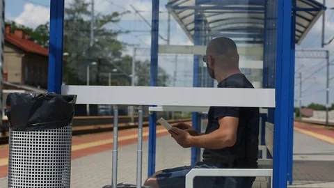 Man browsing internet on tablet while sitting on the train stop and waiting  Stock Footage 78654676