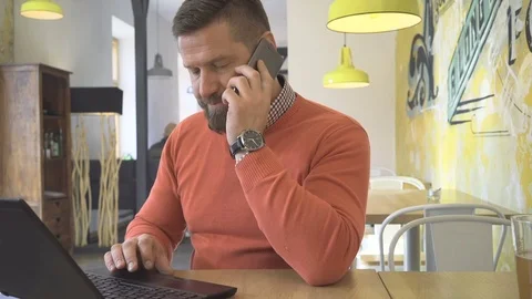 Man browsing laptop computer, talking by smartphone, sitting in cafe 库存影片 73226979