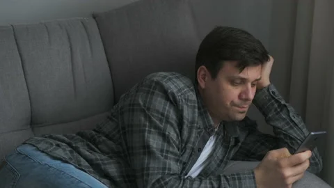 Man is browsing mobile phone typing message lying on couch at home. Stock Footage 158311033