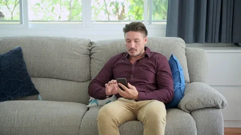 Man browsing phone on couch at home. Focus mood. Stock Footage 105319786