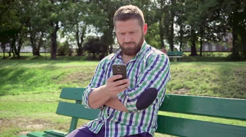 Man browsing smartphone on bench in park. Steadicam. Stock Footage 67235279