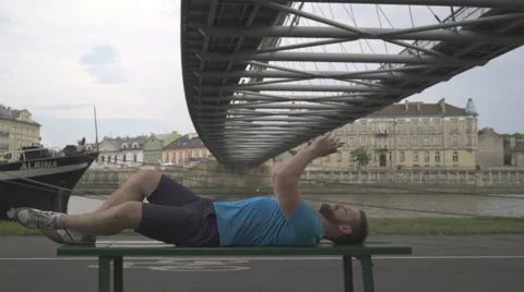 Man is browsing smartphone, lying on the bench against the river. Vídeo Stock 65187852