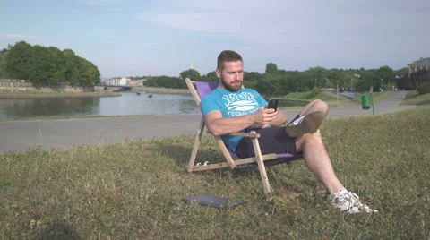 Man is browsing smartphone, lying on sunbed by the river. 動画素材 65205411