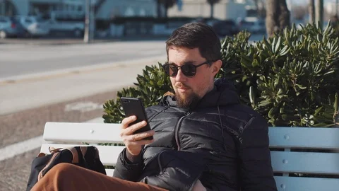 Man is browsing by smartphone sitting outdoors Stock Footage 112651383
