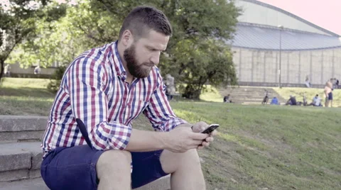 Man browsing smartphone, sitting on stairs. 库存影片 67245582