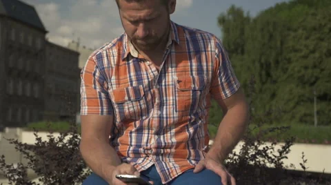 Man browsing smartphone, sitting on wall, tilt shot 動画素材 52713380