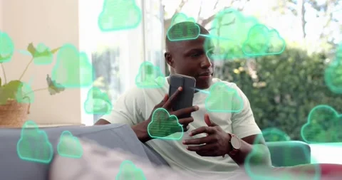 Man browsing smartphone syncing data with green cloud icons around sofa then Video stock 316606565