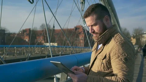 Man browsing tablet computer, answers phone call, on the footbridge, sunset  Video stock 72711383