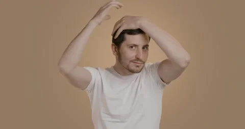 Man with a brunette beard while fixing his hair with a fixing gel. Young man in Stock Footage 232059360