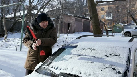 A man brushes a car windshield from snow. In winter, the car was covered with Video stock 150179124