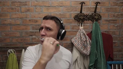 A man brushes his teeth and dances to the music playing in his headphones. Stock Footage 143969516