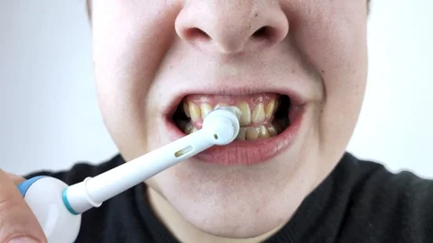 A man brushes his teeth with an electric brush while looking at the camera, as i Stock-Footage 124946755