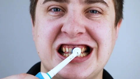 A man brushes his teeth with an electric brush while looking at the camera, as i Stock Footage 124946966