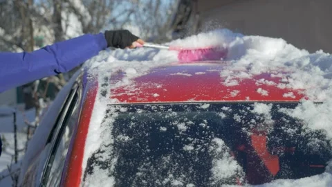 Man brushes packed snow from red car windshield before departure Stock Footage 345605843