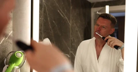 Man brushes teeth with electric toothbrush in bathroom Stock Footage 248310952