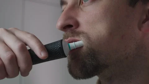Man is brushing his teeth with an electric toothbrush in bathroom as part of his Stock Footage 321426100