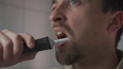 Man brushing his teeth with an electric toothbrush in the bathroom as part of Stock Footage 321426130