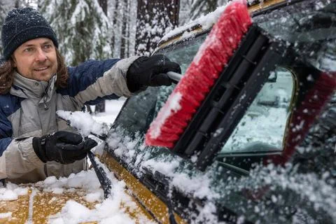 A man is brushing snow off of a car window Stock Photos