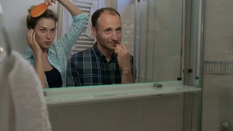 Man brushing teeth and woman combing hair in bathroom. Male carefully cares for Video stock 77495853