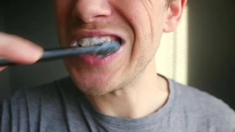 Man brushing teeth with black charcoal toothpaste for whitening Vídeos de archivo 337831074