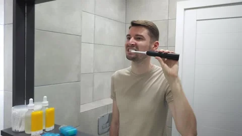 Man brushing teeth with electric toothbrush in bathroom Stock Footage 283931468