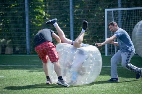 Man in a bubble inside felling upside down on a football field, men helping him Foto stock