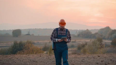 Man builder architect with helmet walks holds tube tablet compuer in field Video stock 169774874