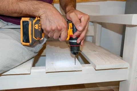 Man Builder Carpenter drilling Cordless hammer Drill Into Wooden Board bench 写真素材
