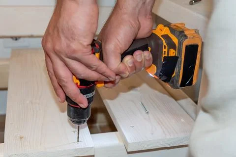 Man Builder Carpenter drilling Cordless hammer Drill Into Wooden Board bench Stockfoto's