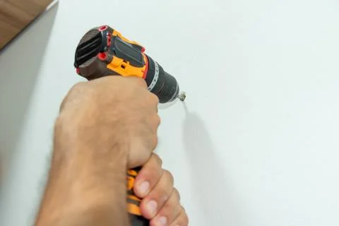 Man Builder Carpenter hammer drilling Cordless Drill Into white concrete wall Photos