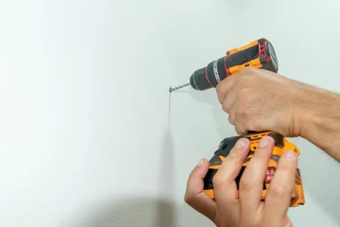 Man Builder Carpenter hammer drilling Cordless Drill Into white concrete wall 库存照片