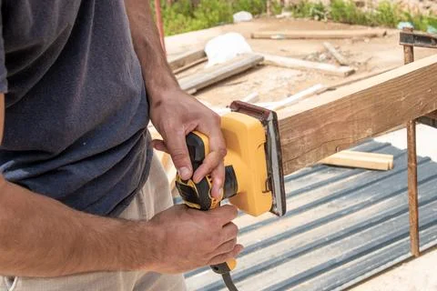 Man Builder Carpenter Sanding Surface Wooden Board Beam With Grinder machine Foto stock