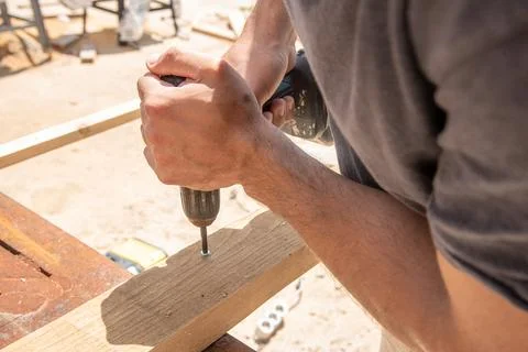Man Builder Carpenter screw driving Cordless Drill In Wooden Board On sawhors Фото
