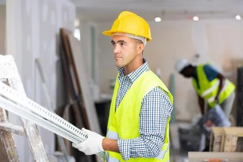 Man builder carrying metallic profile while working in construction site closeup Stock Photos
