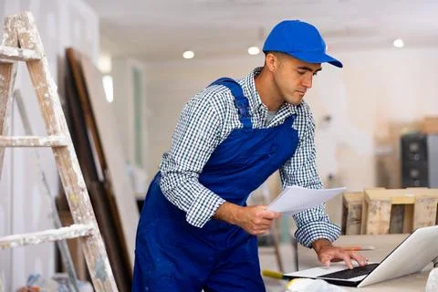 Man builder checking project documentation and using laptop Stock Photos