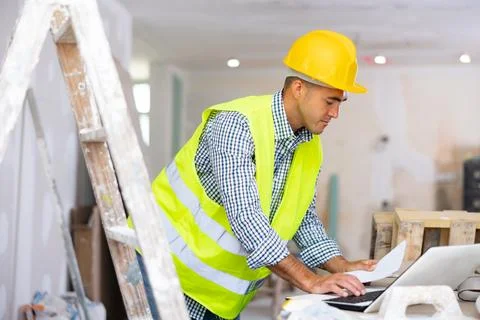 Man builder checking project documentation and using laptop Foto stock