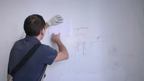 Man builder compares scheme on wall and renovation plan Stock Footage 151784295