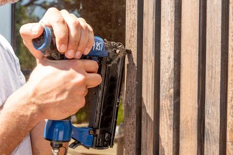 Man Builder craftsman Carpenter hammers nails on Wooden Board Beam With finis Fotos Stock