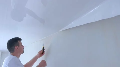 Man builder dismantling of stretch suspended ceiling cutting it using knife. Stock Footage 136931965