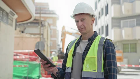 Man builder in hardhat and reflective vest checks tablet and smiles, hand o.. Stock Footage 339177885