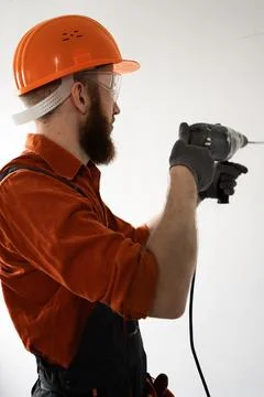 Man builder in hardhat drilling wall with drill perforator Stock Photos
