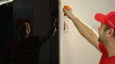 A man, a Builder in a red cap, sprays liquid on black glass doors 스톡 동영상 113530698