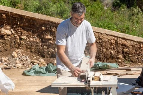Man builder saws and grinds wooden boards, carpenter craft works with power e 库存照片