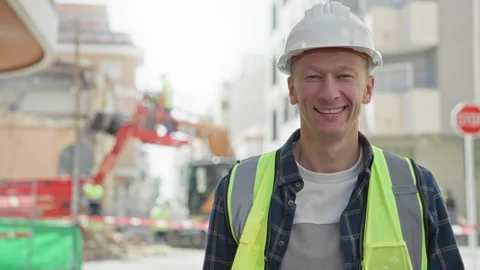 Man builder smiling in hardhat and high visibility vest on street construct.. Vídeos de archivo 339177811