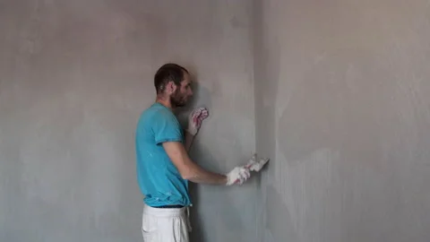 Man Builder Works with Trowel. Smooths Fresh Plaster on Wall. Renovation in Room Stock Footage 168354300