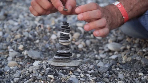 The man is building the balancing stone tower on the beach Stock Footage 88012735